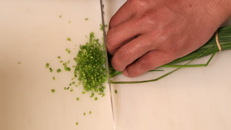 hands of a skilled chef slices the green onion chives quickly with a knife on a chopping board in the kitchen