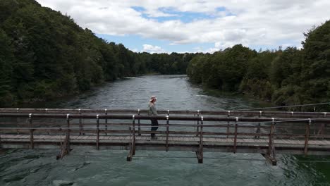 Aerial-side-view-of-a-young-man-wearing-hat-and-walking-on-Rainbow-bridge-at-the-beginning-of-Kepler-Track-in-New-Zealand