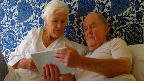 Front-view-of-Caucasian-senior-couple-discussing-over-digital-tablet-on-bed-at-comfortable-home-4k