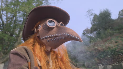 redhead wearing plague mask and cowboy hat breathing out smoke while sat in parkland