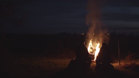 2 men talking next to a big campfire at night