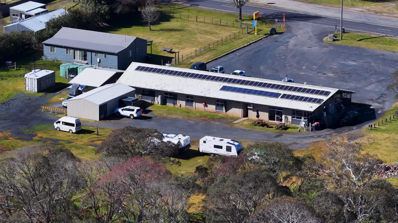 Aerial camera pans across rural motel, caravan park, and solar panels in bright daylight