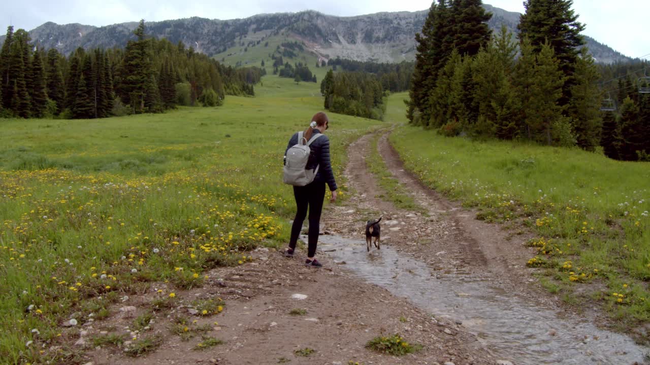 mujer caminando con un pequeño perro negro en un camino de tierra en las montañas