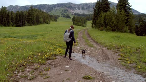 woman walking with small black dog on a dirt road in the mountains