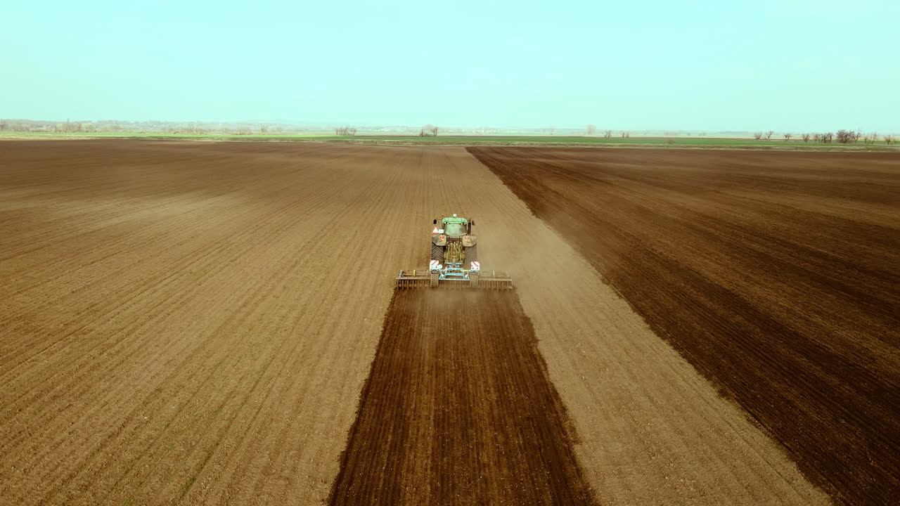 Tractor processes large barren farmland, high angle shot.
