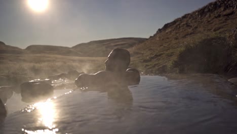 a serene shot captures a man, partially obscured by rising steam, relaxing in the natural waters of hrunalaug hot spring in iceland