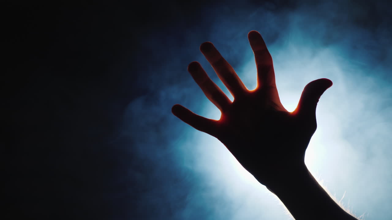 la silueta de la mano de un hombre en la oscuridad de los dedos vienen los rayos de luz