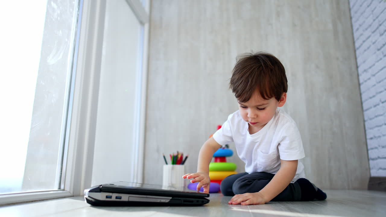 A little boy sits on the floor and draws with colored pencils. The child is engaged in creativity at home.