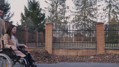 side view of a man taking her disabled friend in wheelchair on a walk around the city