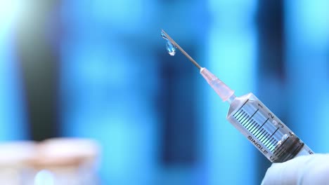 A-syringe-and-needle-drips-with-with-medication-or-a-vaccine-against-a-blue-background