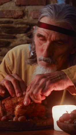 un noble hambriento arranca una pierna de pollo en una cena medieval. un aristócrata maduro come carne de pollo y uva en la mesa de la taberna. un invitado al banquete del rey