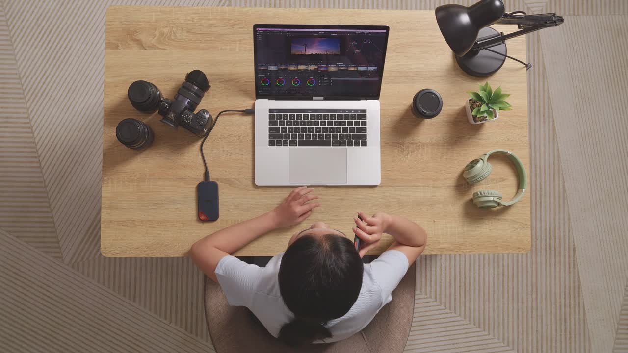집에서 비디오를 편집하는 카메라 에 노트북을 사용하여 작업 공간에 앉아있는 동안 스마트폰에서 이야기하는 여성 색상 등급의 상단 뷰