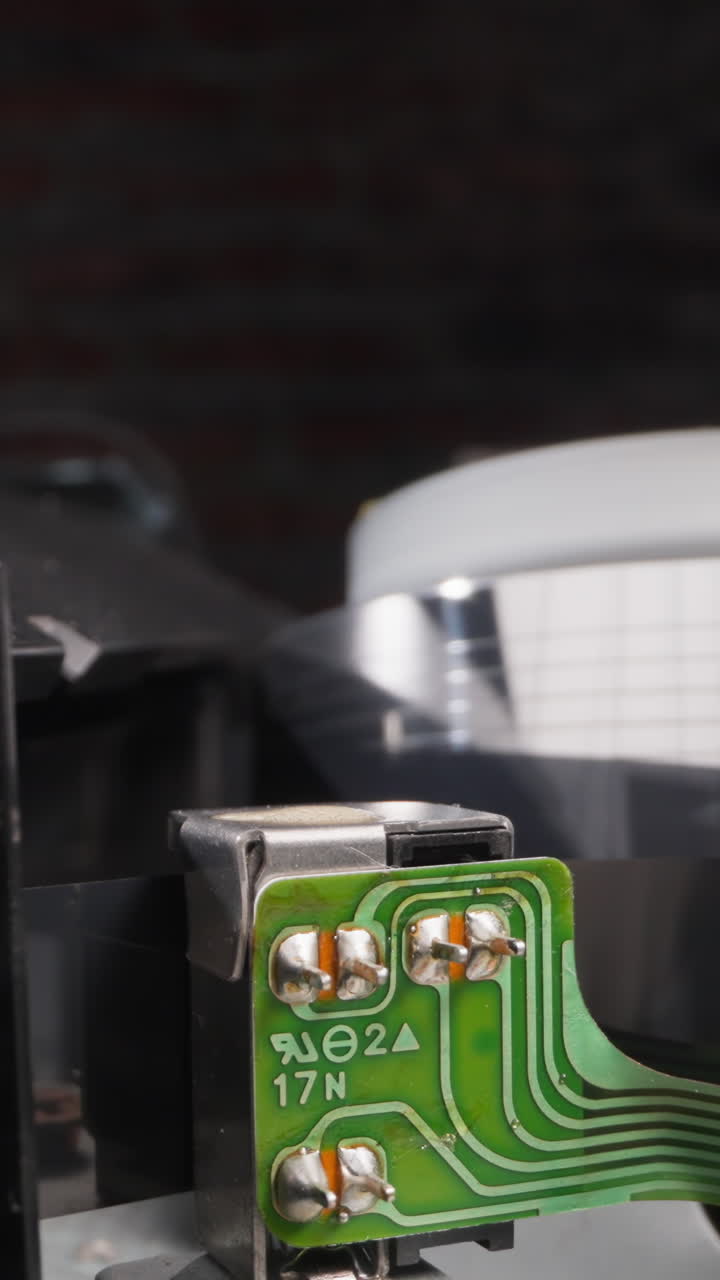 Tape moves through mechanism of videocassette recorder against reading head in room macro view. Vintage device operates with strip to play video