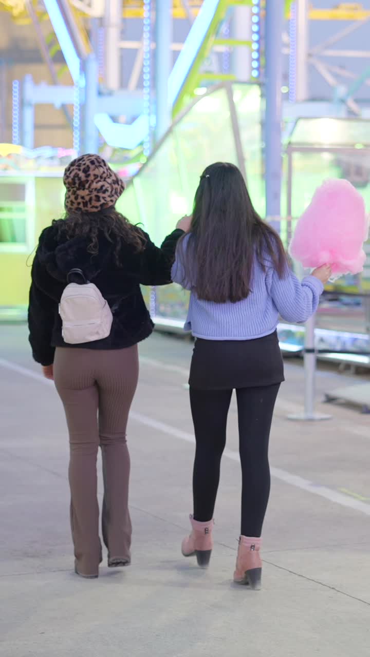 Two women walking at an amusement park at night, one holding cotton candy