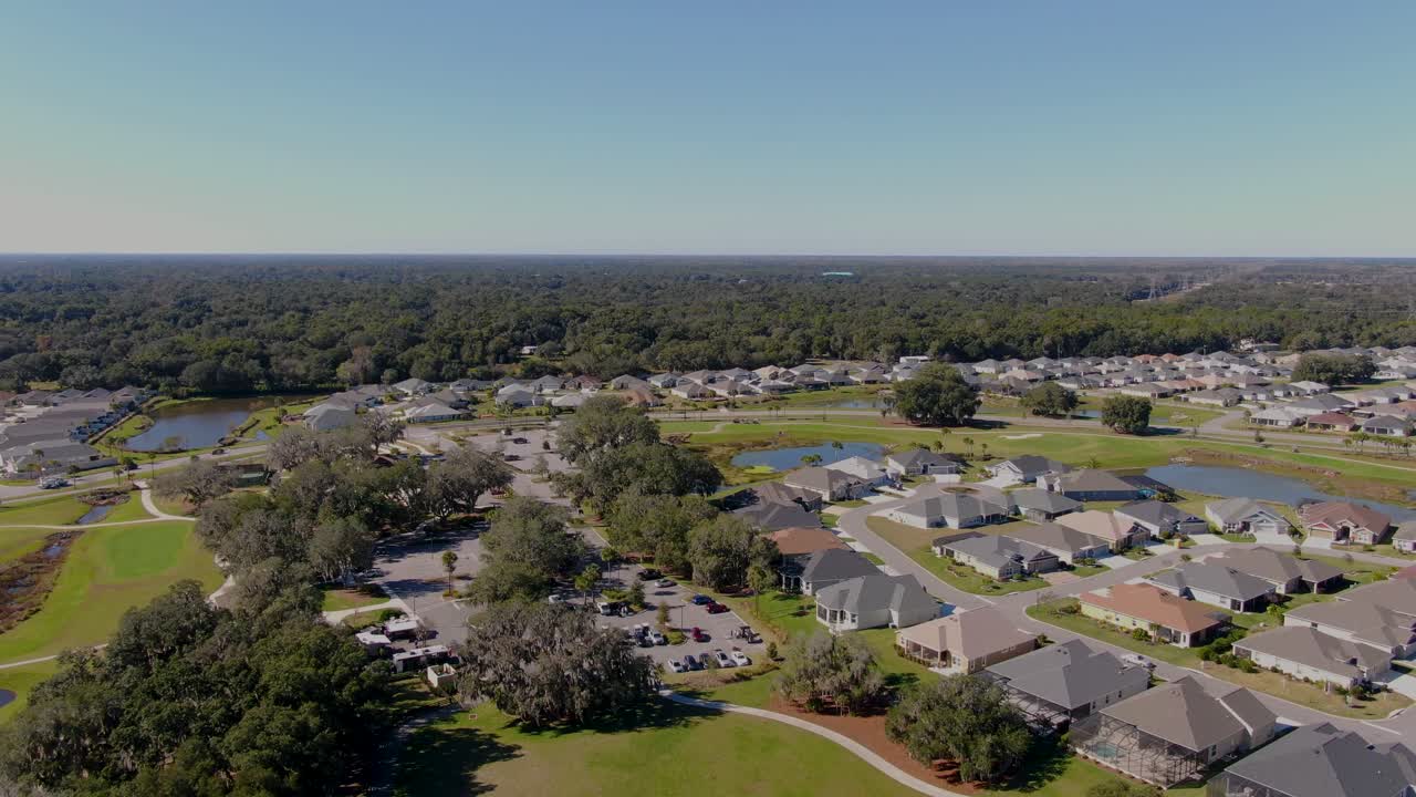 Ripresa a volo di drone dall'alto su Edna’s on the Green a The Villages, in Florida, che mostra i vicini quartieri residenziali, gli spazi verdi, gli stagni e la foresta distante sotto un cielo sereno