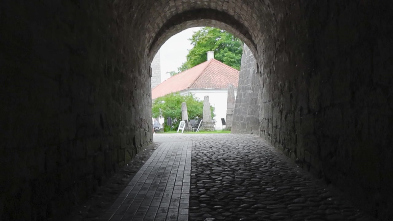 Il filmato mostra un'arcata in pietra con un passaggio a tunnel che conduce a un cortile aperto nel castello di Kuressaare durante l'estate in 4K. Luce del giorno alla fine del tunnel e un edificio medievale sullo sfondo.