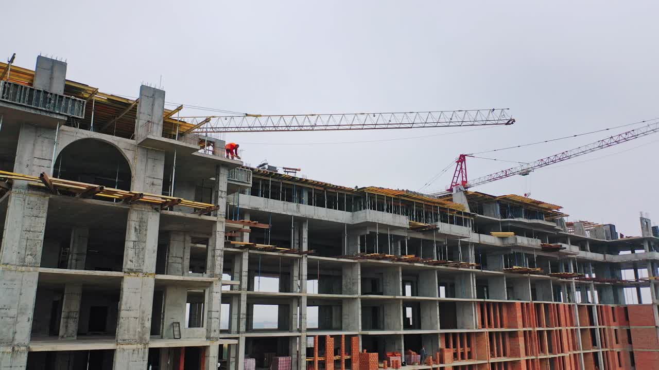 Drone view on a new construction site. Working process of construction the modern building on the background of two big cranes in the city.