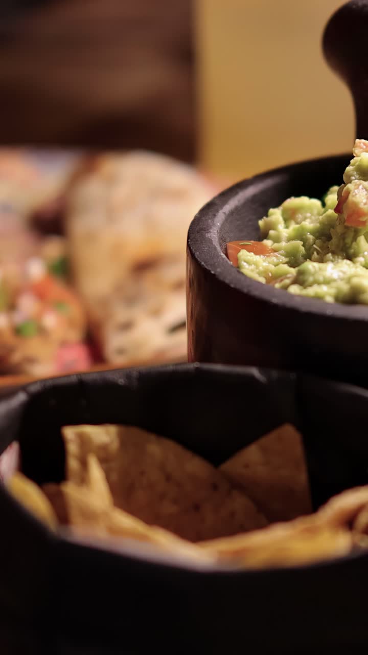Sequenza ravvicinata di mani che preparano e servono quesadilla grigliata con condimenti vivaci, guacamole in una ciotola di pietra e tortilla chips sotto un'illuminazione calda e soffusa.