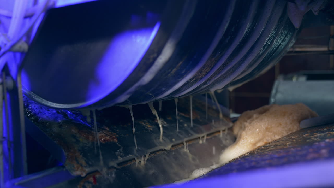 Automated line for production healthy food products. Rotating mechanism at a food factory with fresh juice dripping from it. Close up.