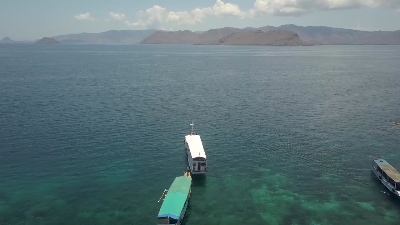 인도네시아 코모도 섬에 있는 핑크 해변 연안의 목가적인 바다에서 작은 순항 보트 - 공중 비행 샷