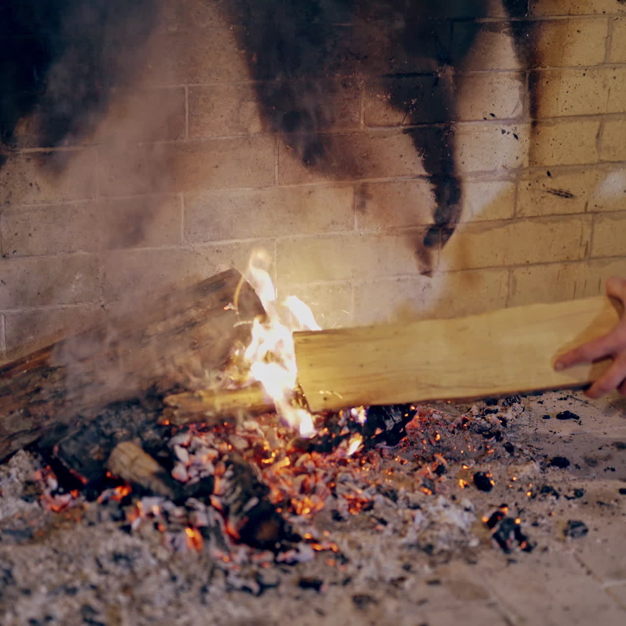 Male's hands split the heat with a log in the fire indoors. Close-up hands of a man putting wood into fire in fireplace and then warming up his cold hands. Christmas time.