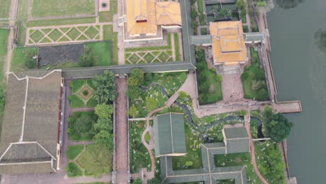 vista aérea de drones en vietnam volando sobre la muralla de la fortaleza de ladrillo de piedra imperial, jardines verdes, templos y pequeños edificios en un día nublado y brumoso