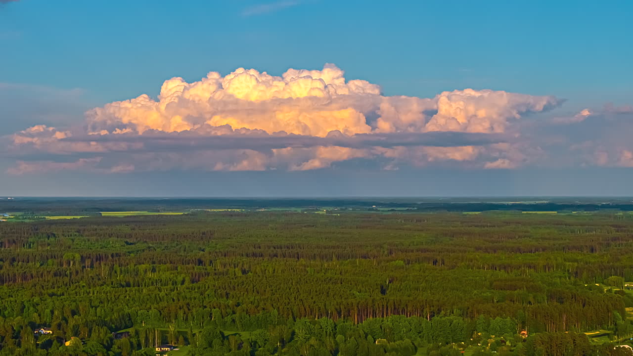 Towering cumulus clouds over dense green forest under dramatic sky in aerial timelapse