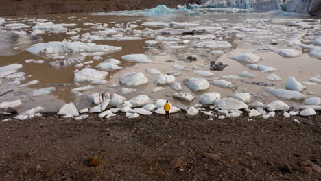 Aerial:-Flyover-of-one-man-standing-on-the-bank-of-Svinafellsjokull-glacier-lagoon-in-Iceland