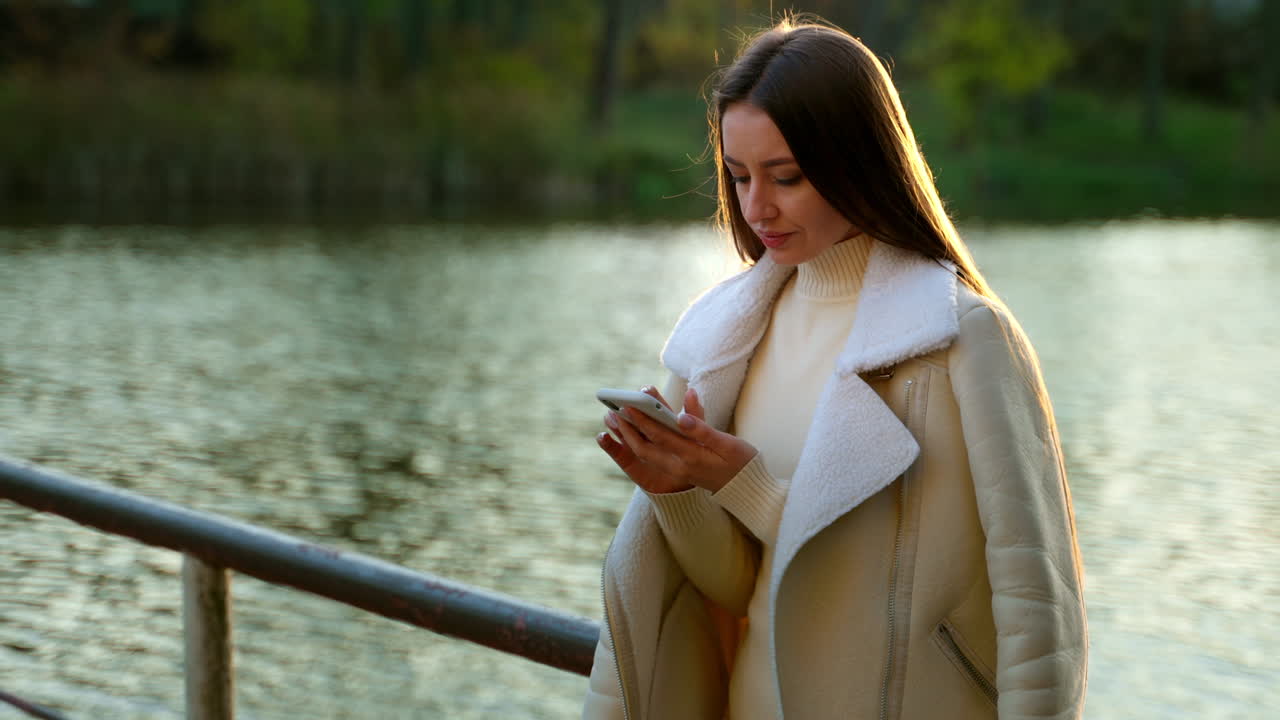 Woman using phone in a park by a lake