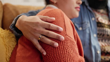 una pareja sentada en un sofá, una persona con el brazo alrededor del hombro de la otra.