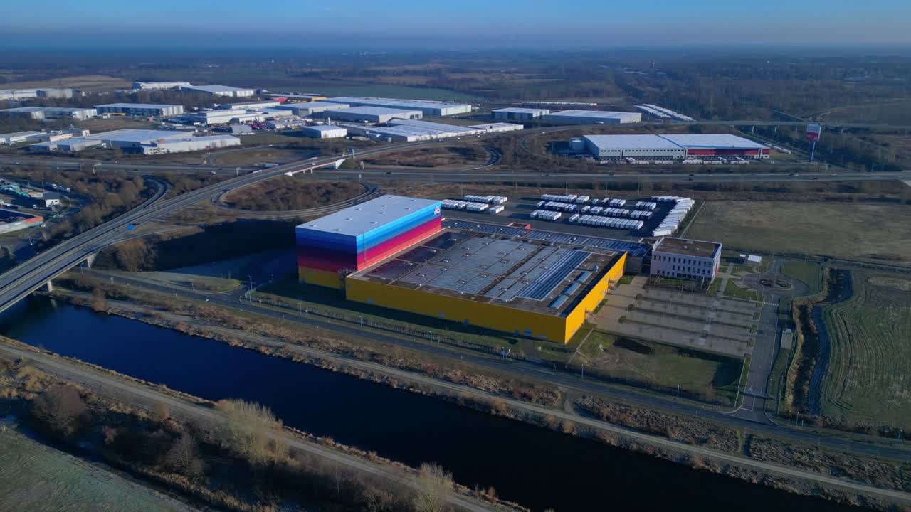 panorama of logistics center and distribution warehouse serving the drugstore chain, positioned next to a canal and highway infrastructure. Best aerial view ascending raise up drone