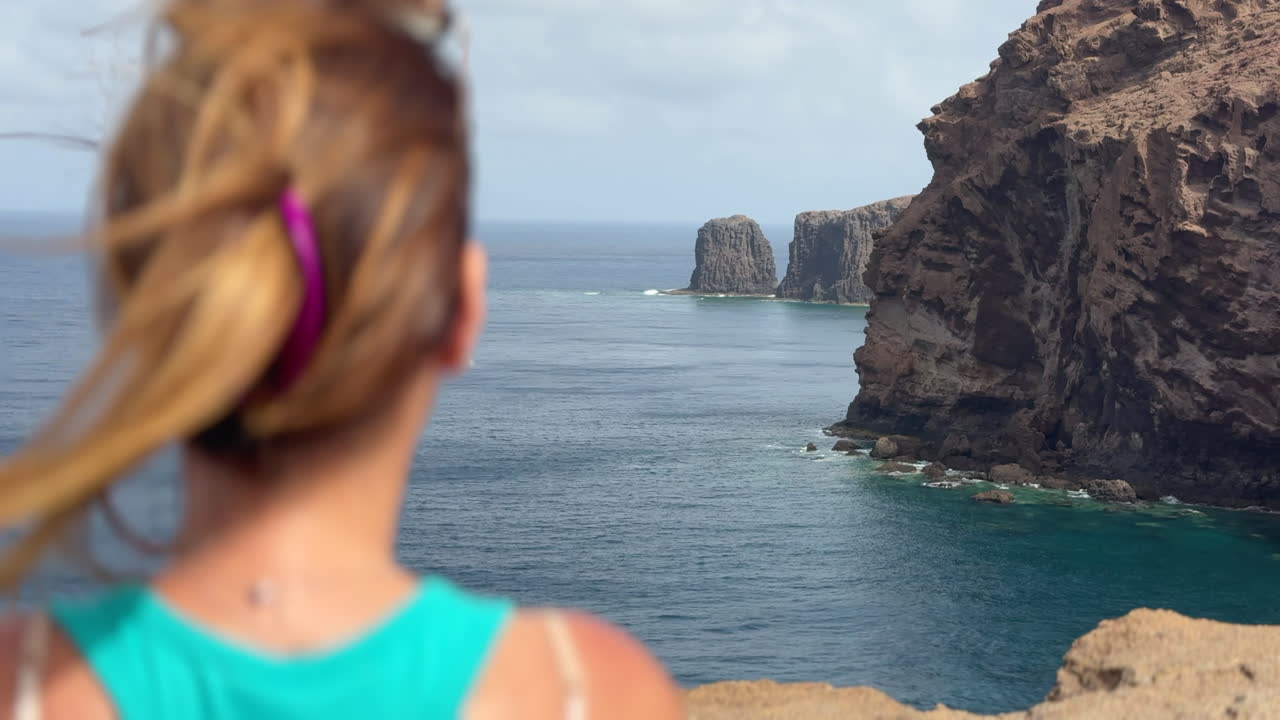 Tourist observing Roque Partido from Gran Canaria's coast, enjoying breathtaking ocean and cliff views