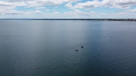 Drone-flying-over-fishing-boats-on-the-ocean,-coastline-in-the-background