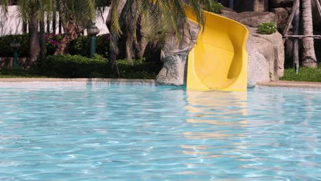 a yellow water slide descends into a clear blue pool