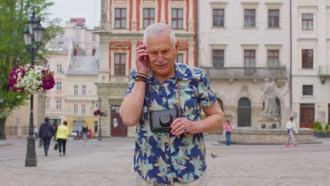 Älterer-Alter-Tourist-In-Stilvoller-Kleidung,-Der-Beim-Spazierengehen-Auf-Der-Stadtstraße-Mit-Dem-Mobiltelefon-Telefoniert