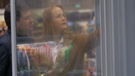 young couple picking food from the store freezer