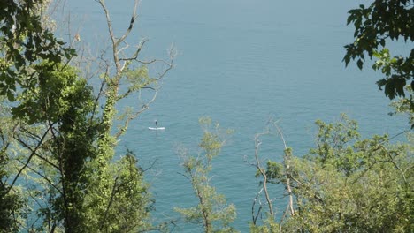 Person-standing-paddling-in-canoe-on-a-lake-in-the-alps-seen-through-the-forest