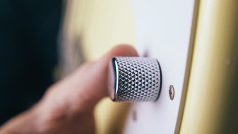 le doigt tourne le bouton de contrôle de volume argenté sur la guitare basse