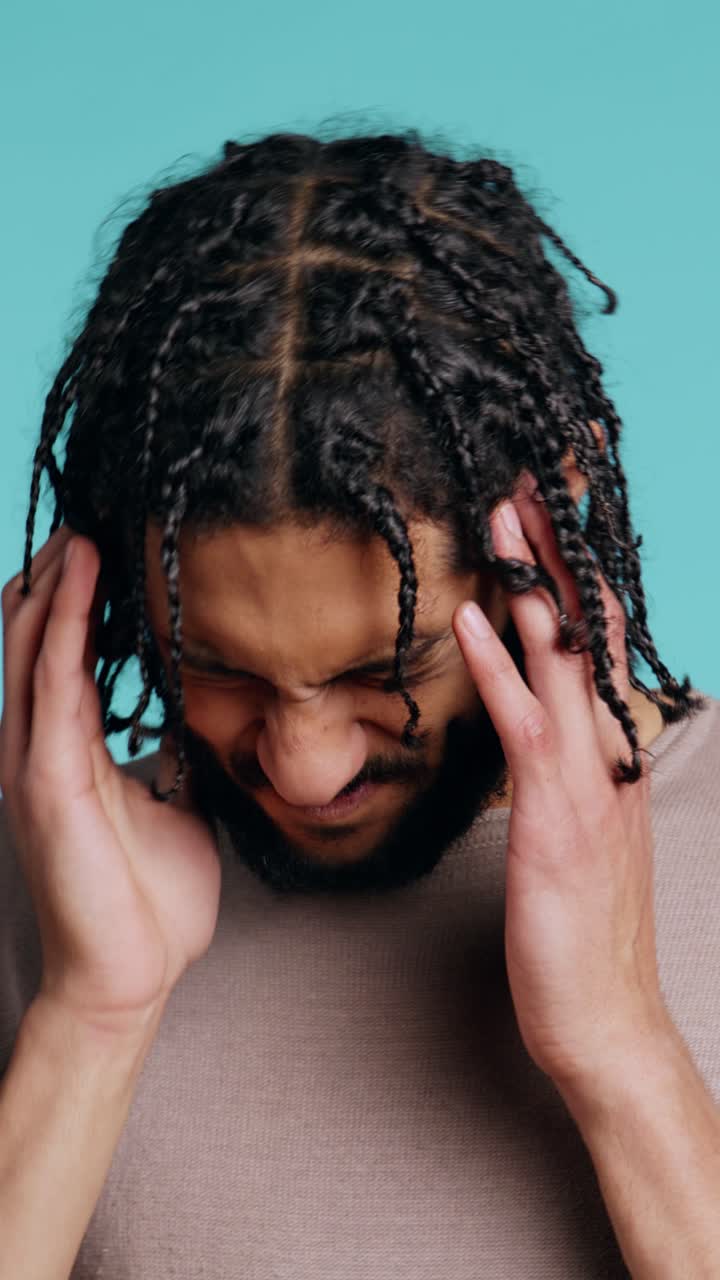 Vertical video Man wincing from pain, suffering from headache, studio background