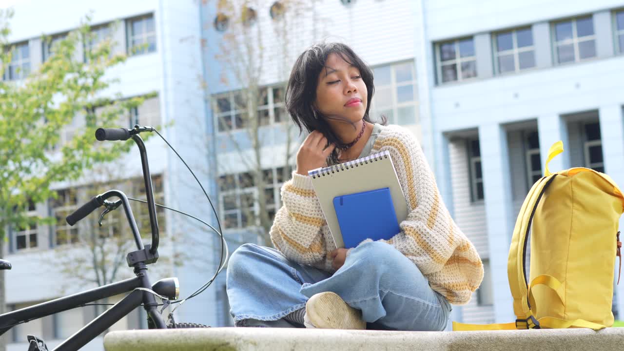 A student sitting on campus with her bicycle and books