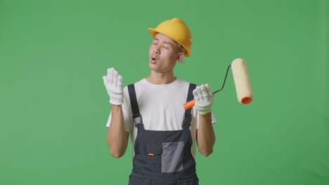 wondering asian man painter wearing safety helmet saying why and standing doubtfully in the green screen background studio