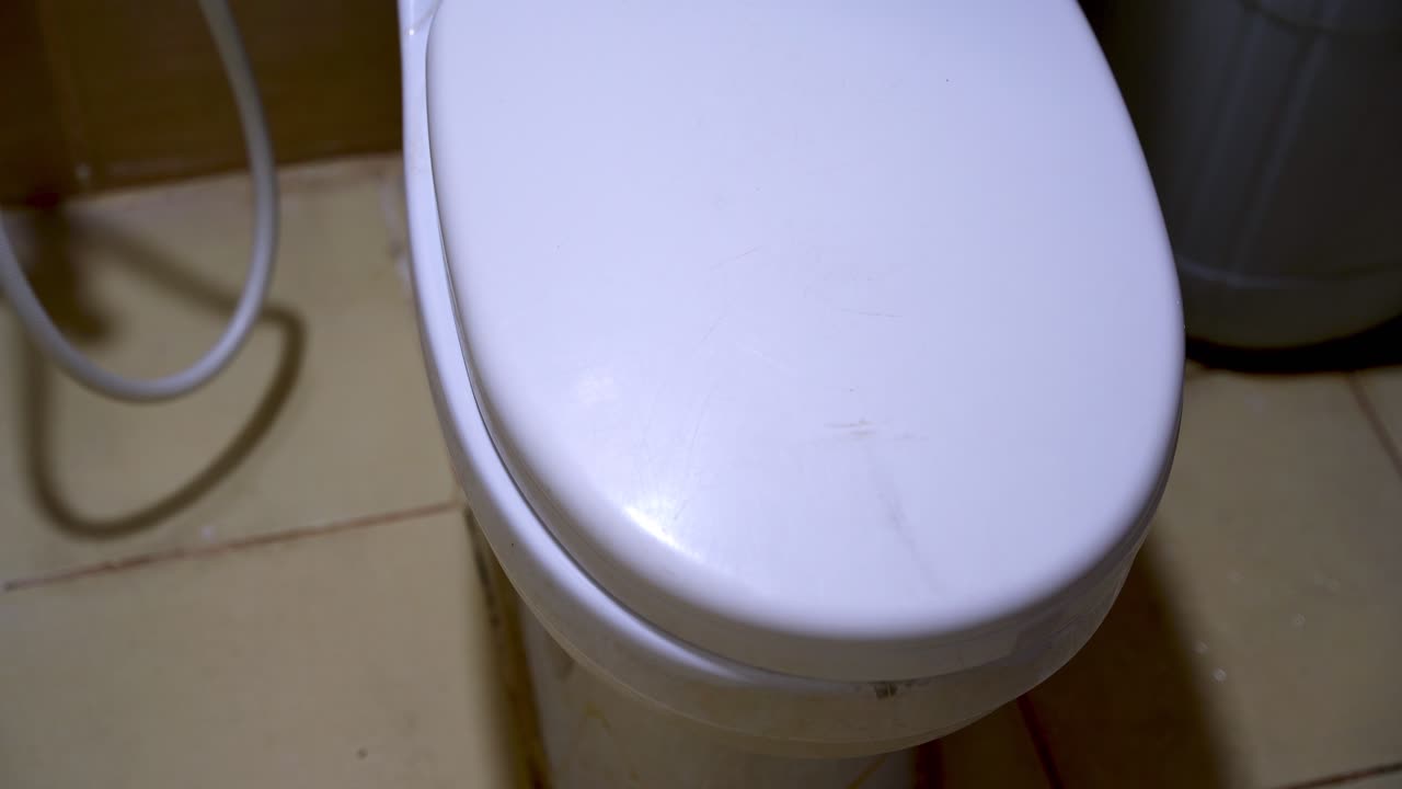 Close-up of a hand lifting and lowering a white ceramic toilet seat lid. Demonstrating proper bathroom hygiene and etiquette by closing the lid to prevent germ spread