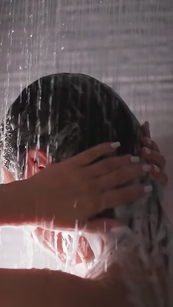 Woman washes hair with shower water closeup. Elegant lady cleans head from foam in bathroom. Woman enjoys routine hygienic procedures at home