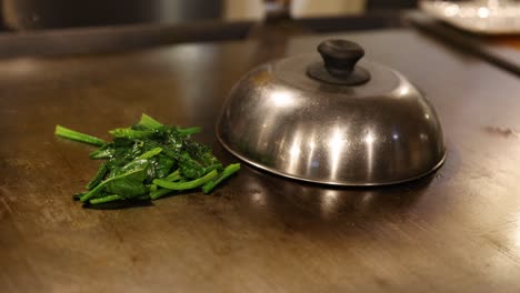 espinacas desveladas de debajo de una clocha de metal en la mesa.