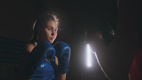 boxeadora golpeando unos guantes de enfoque con guantes de boxeo en un gimnasio ahumado