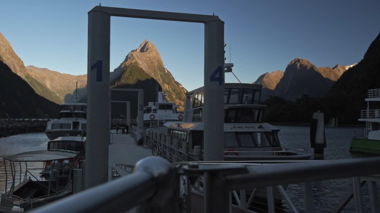 Wide angle view of the  Milford Sound in New Zealand. Light of the sunrise on the mountains, boats at the habor of the sound in the foreground