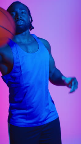 retrato vertical de estudio de video de un jugador de baloncesto masculino con chaleco de equipo lanzando y atrapando la pelota contra una iluminación mixta de clave baja colorida 1