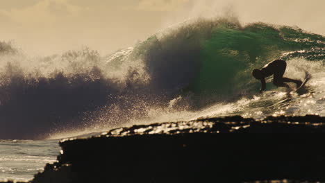 slow motion view of surfer dropping in on golden wave with light sparkling as they cutback and spray crouching down low
