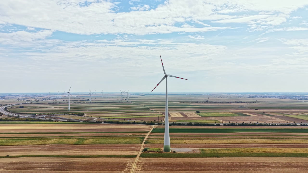 Wind turbines stand tall in a wide field under a bright sky with clouds in the background during the day time