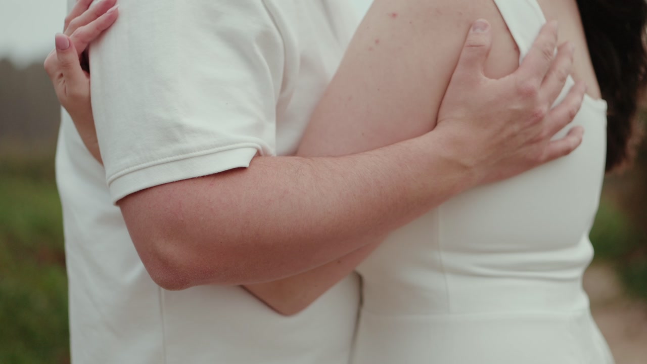 Close view of couple embracing with hands on shoulders and back during outdoor wedding moment